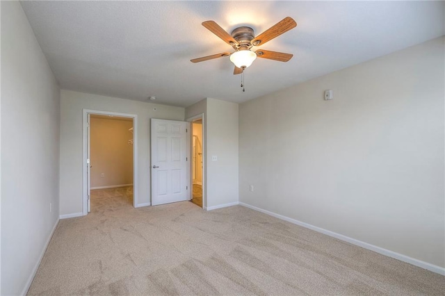 unfurnished bedroom featuring light colored carpet, baseboards, ceiling fan, and a spacious closet