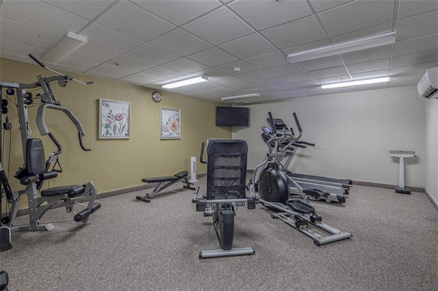 exercise room featuring an AC wall unit, baseboards, a drop ceiling, and carpet