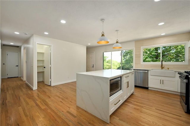 3907 Scherer Rd, Lees Summit, MO 64082 - kitchen featuring a kitchen island, white cabinetry, a sink, light wood-style flooring, and appliances with stainless steel finishes