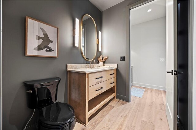 bathroom featuring vanity, wood finished floors, toilet, baseboards, and recessed lighting