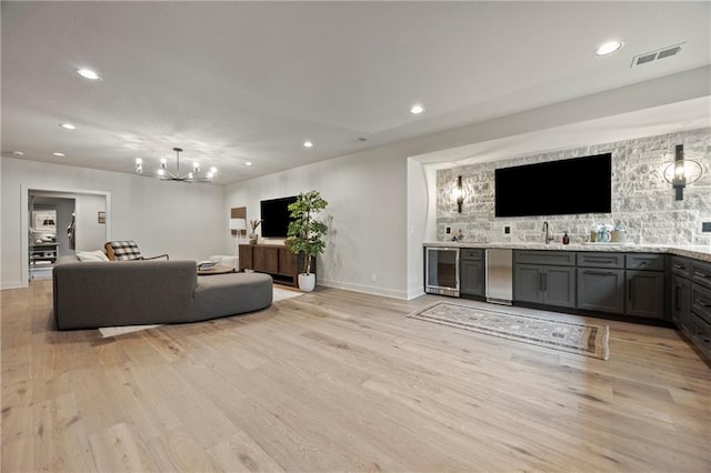 living area featuring visible vents, light wood-style flooring, wine cooler, and a notable chandelier
