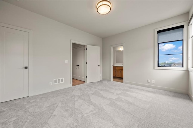 unfurnished bedroom with visible vents, carpet flooring, baseboards, and ensuite bath