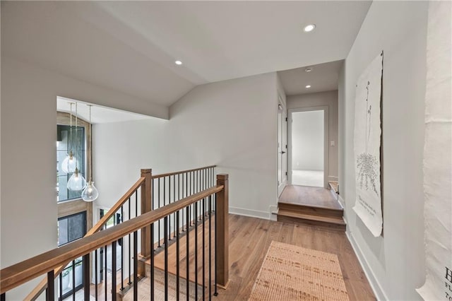 hall featuring vaulted ceiling, recessed lighting, wood finished floors, and an upstairs landing