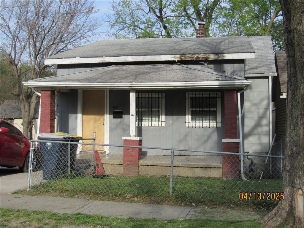 view of front facade featuring covered porch, a shingled roof, a chimney, and a fenced front yard