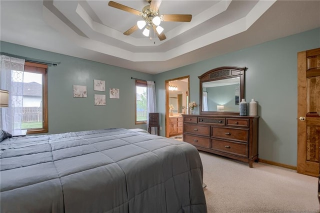 bedroom featuring ceiling fan, a raised ceiling, baseboards, ensuite bathroom, and light carpet