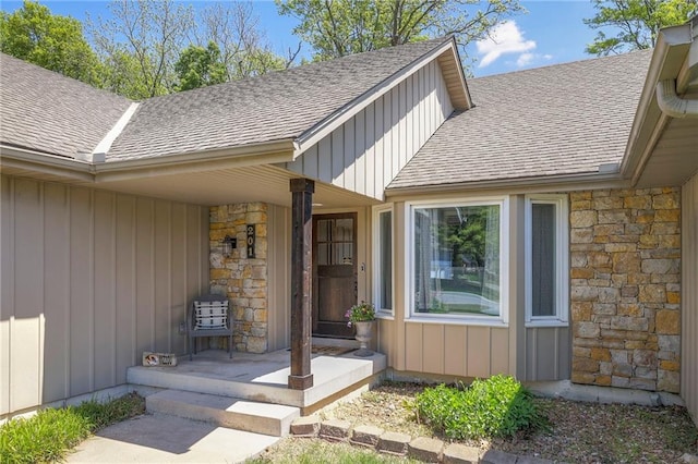 doorway to property with stone siding, roof with shingles, board and batten siding, and covered porch