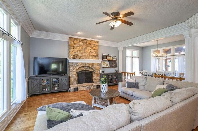 living room with ornate columns, a ceiling fan, a chandelier, crown molding, and a fireplace