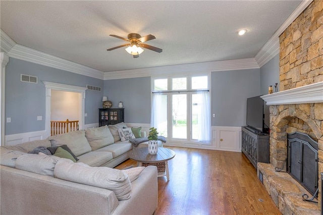 living area featuring ceiling fan, a fireplace, wood finished floors, wainscoting, and crown molding