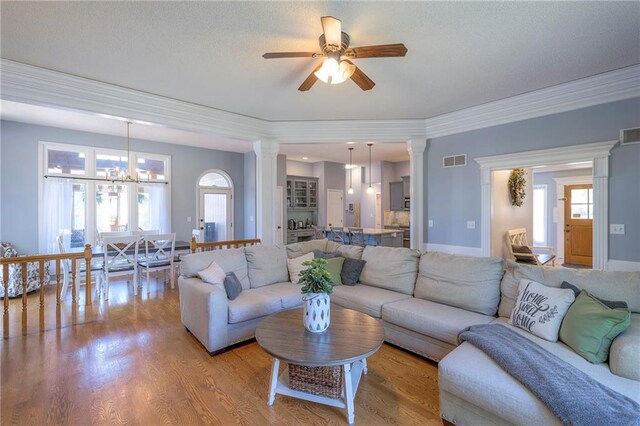 living area featuring a ceiling fan, decorative columns, light wood-style flooring, and crown molding