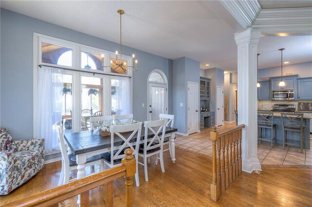 dining room with decorative columns, light wood-style floors, a chandelier, a textured ceiling, and baseboards