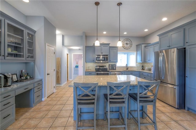 kitchen with stainless steel appliances, a sink, light stone countertops, a kitchen island, and light tile patterned flooring