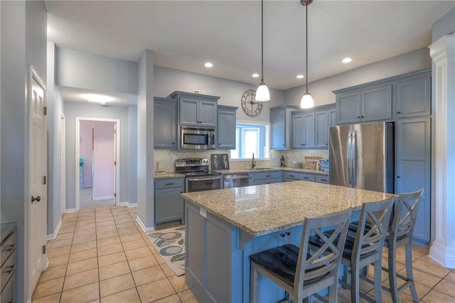 kitchen with stainless steel appliances, a sink, a breakfast bar area, light stone counters, and light tile patterned floors