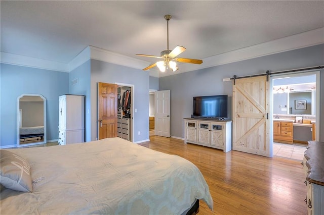 bedroom featuring ornamental molding, a barn door, light wood-style floors, baseboards, and a walk in closet