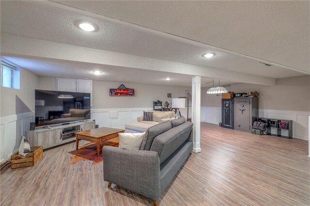 living room featuring a wainscoted wall, a decorative wall, a textured ceiling, and light wood-style floors