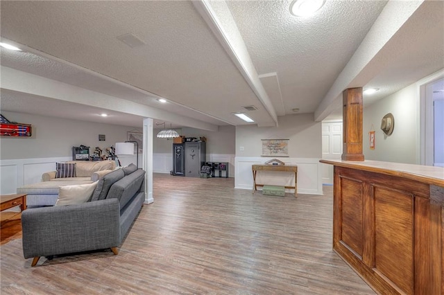 living area with a textured ceiling, light wood-style flooring, a decorative wall, a wainscoted wall, and ornate columns