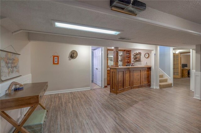 indoor bar featuring light wood-style flooring, stairway, a textured ceiling, and baseboards