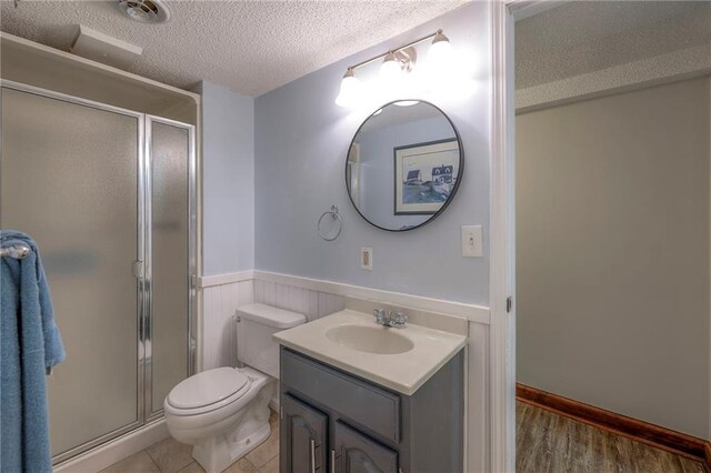 full bath with wainscoting, a textured ceiling, toilet, a shower stall, and vanity