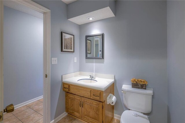 half bath featuring toilet, tile patterned floors, baseboards, and vanity