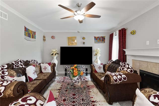 carpeted living room with a ceiling fan, visible vents, a fireplace, baseboards, and ornamental molding