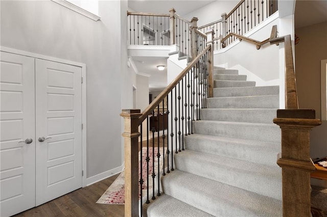 stairway with baseboards, wood finished floors, and a towering ceiling