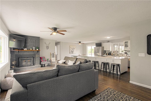 1204 E 223rd St, Cleveland, MO 64734 - living room featuring a brick fireplace, baseboards, ceiling fan, dark wood-style floors, and a textured ceiling