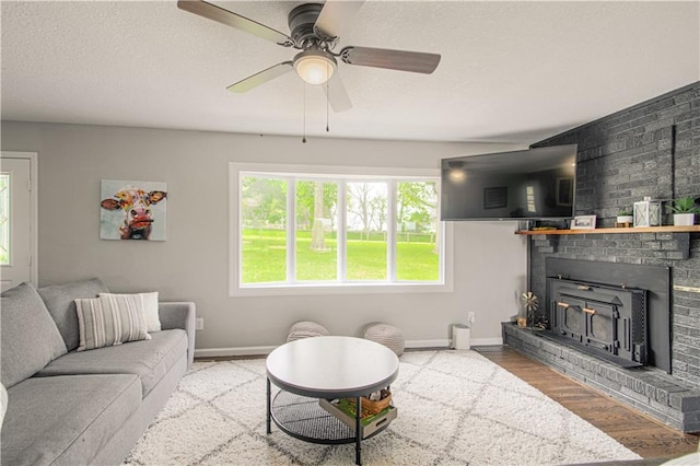 1204 E 223rd St, Cleveland, MO 64734 - living room featuring a brick fireplace, a textured ceiling, a ceiling fan, baseboards, and wood finished floors