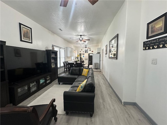 living area featuring light wood-style floors, a textured ceiling, baseboards, and ceiling fan