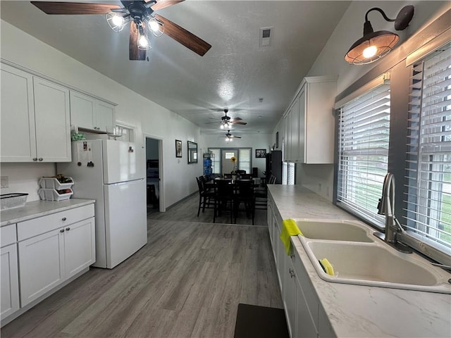 kitchen with white cabinets, ceiling fan, a sink, freestanding refrigerator, and light wood-type flooring