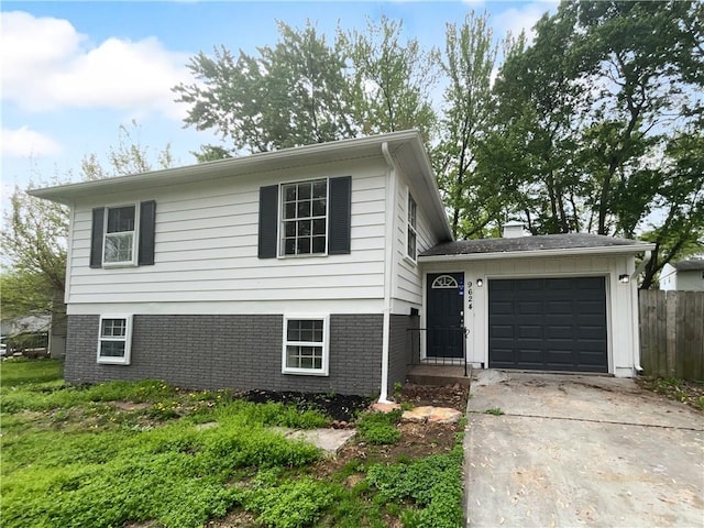 tri-level home with concrete driveway, brick siding, fence, and a garage