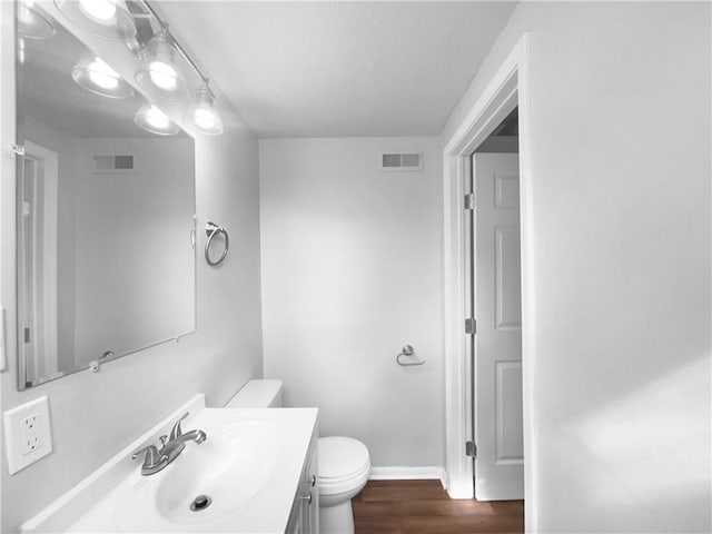 bathroom with vanity, toilet, wood finished floors, and visible vents