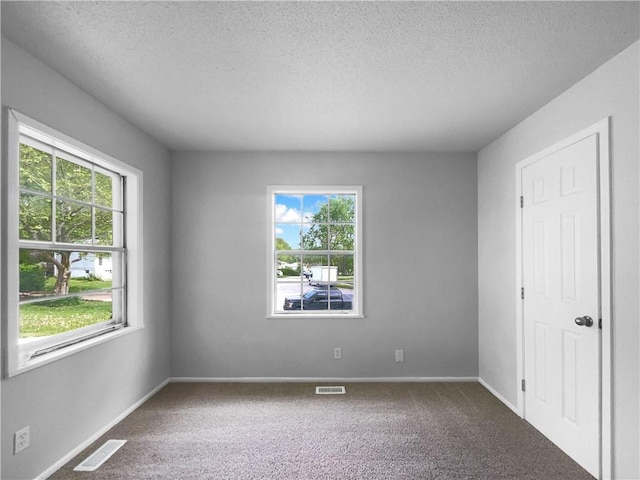 empty room featuring visible vents, carpet flooring, and a textured ceiling