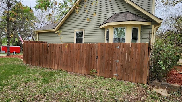 view of home's exterior with a lawn, roof with shingles, and fence