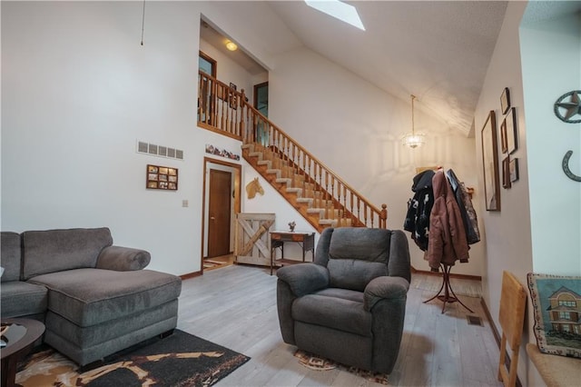 living area with stairway, high vaulted ceiling, wood finished floors, and visible vents