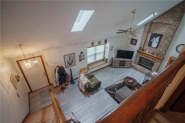 living room with ceiling fan, a fireplace, lofted ceiling with skylight, and wood finished floors