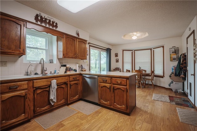 kitchen featuring a textured ceiling, light wood-type flooring, dishwasher, a sink, and a peninsula
