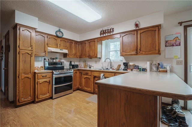 kitchen featuring a sink, brown cabinets, a peninsula, and range with two ovens
