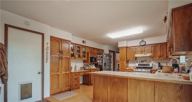 kitchen with visible vents, a peninsula, a textured ceiling, under cabinet range hood, and appliances with stainless steel finishes