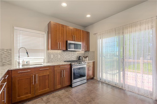 4515 67th Ter, Kansas City, MO 64119 - kitchen featuring appliances with stainless steel finishes, a sink, brown cabinets, decorative backsplash, and light stone countertops