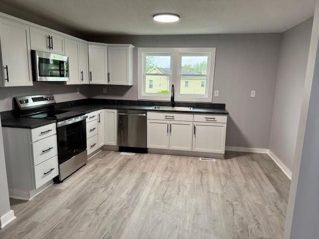 403 W Cedar St, Waverly, MO 64096 - kitchen with stainless steel appliances, a sink, light wood-type flooring, and dark countertops
