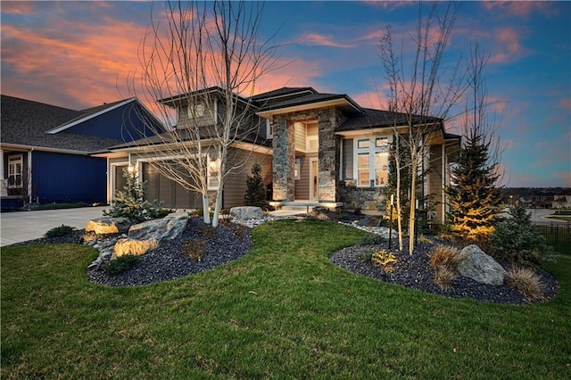 prairie-style house with a garage, a front yard, driveway, and stone siding
