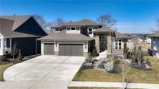 prairie-style home with roof with shingles, an attached garage, concrete driveway, and stone siding