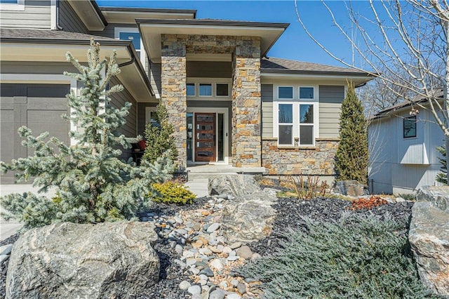 entrance to property featuring a garage, roof with shingles, and stone siding
