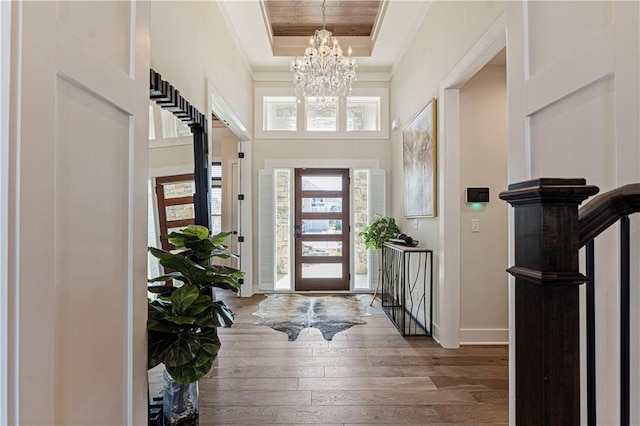 entryway with hardwood / wood-style flooring, baseboards, a chandelier, ornamental molding, and a tray ceiling