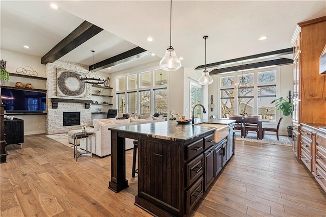 kitchen with a sink, wood-type flooring, an island with sink, wall oven, and a kitchen bar