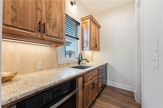 kitchen featuring dark wood-style flooring, light stone countertops, baseboards, a sink, and backsplash