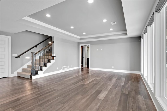 unfurnished living room with visible vents, wood finished floors, baseboards, a tray ceiling, and stairs