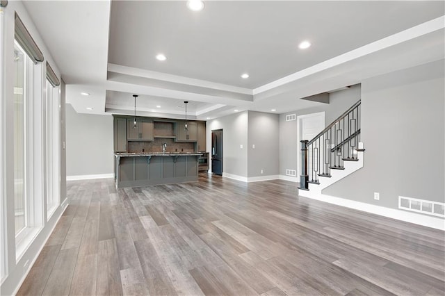 unfurnished living room featuring visible vents, stairway, a raised ceiling, baseboards, and light wood-style flooring