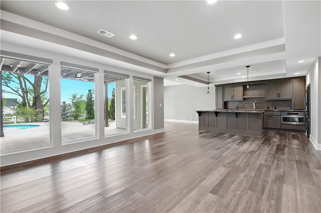 living area with visible vents, wood finished floors, baseboards, recessed lighting, and a raised ceiling