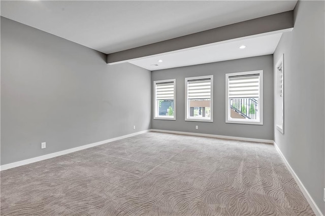 empty room with carpet floors, baseboards, plenty of natural light, and beamed ceiling