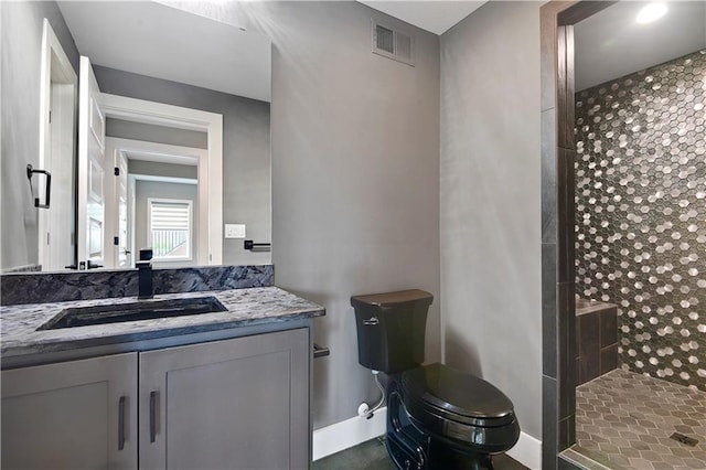 full bath with visible vents, vanity, toilet, baseboards, and a tile shower